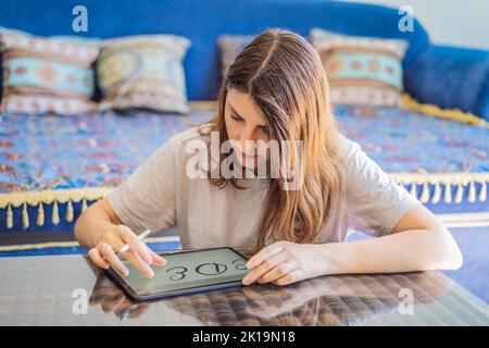 Calligrapher Young Woman writes phrase on digital tablet. Inscribing ornamental decorated letters. Calligraphy, graphic design, lettering, handwriting Stock Photo