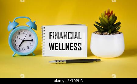 Financial wellbeing text written on notepad and yellow background with clock and cactus Stock Photo