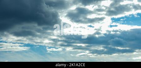 Blue sky with thunderclouds. The sun breaks through the clouds. Black clouds. Banner. Stock Photo