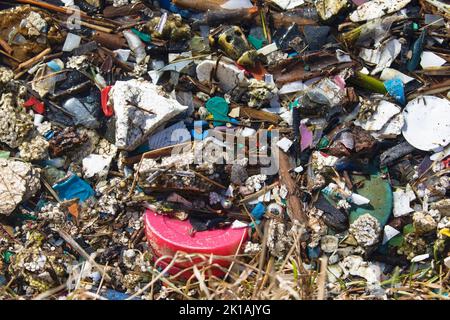 Plastic waste and other trash dumped and carried through a city drainage system where it washed up on the shore of a stormwater treatment pond Stock Photo