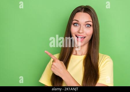 Portrait of positive impressed girl with straight hairdo dressed yellow t-shirt indicating empty space isolated on green color background Stock Photo