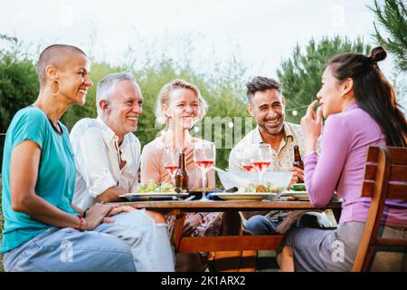 Group of adult friends or familly talking and having fun sitting at table in a dinner party in a back yard. Lifestyle concept. Stock Photo
