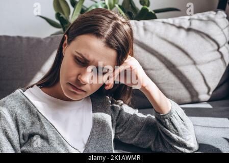 Close-up of lonely single frustrated female. Lost on sad thoughts millennial woman sit on grey sofa at home feels emptiness by personal difficulties a Stock Photo