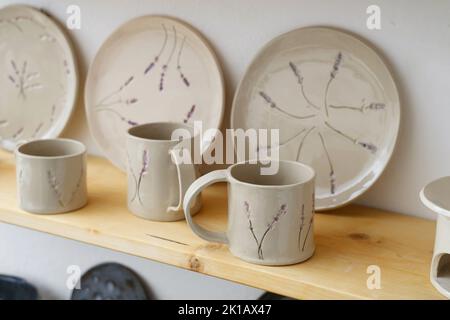 Ceramics with floral and natural patterns on the shelf of the shop. Creative minimalistic handmade cups, mugs and plates. Pottery cutlery earthly Stock Photo