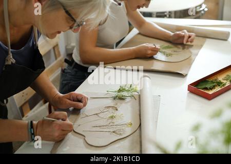 Pottery workshop in studio. master working with clay on the table. Adults learning to do ceramic plates. Pottery as hobby and leisure activity Stock Photo