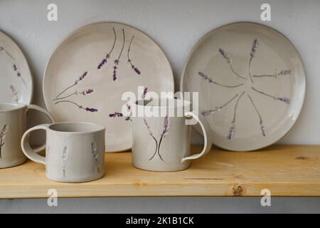 Ceramics with floral and natural patterns on the shelf of the shop. Creative minimalistic handmade cups, mugs and plates. Pottery cutlery earthly Stock Photo
