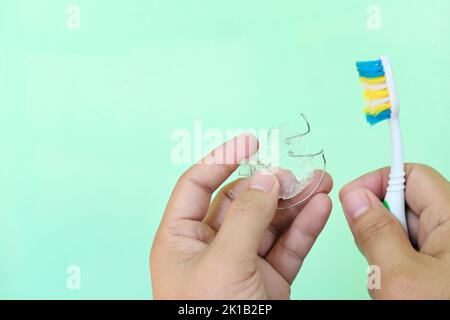 Retainer cleaning care and maintenance concept. Hand holding hawley dental retainers and a toothbrush with copy space. Stock Photo