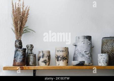 Ceramics with floral and natural patterns on the shelf of the shop. Creative minimalistic handmade cups, mugs and plates. Pottery cutlery earthly Stock Photo