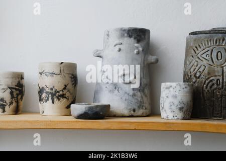 Ceramics with floral and natural patterns on the shelf of the shop. Creative minimalistic handmade cups, mugs and plates. Pottery cutlery earthly Stock Photo