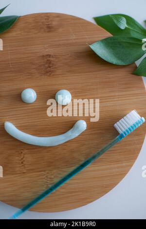 Smiling face made of toothpaste, brush on wooden background with green leaves, flat lay. High quality photo Stock Photo