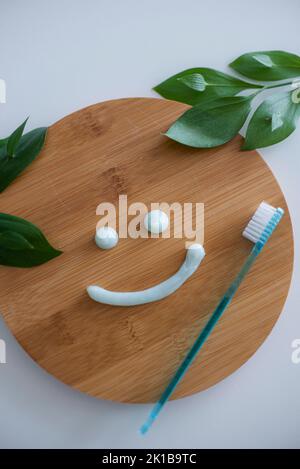 Smiling face made of toothpaste, brush on wooden background with green leaves, flat lay. High quality photo Stock Photo