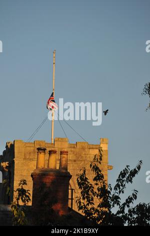 Church with flag half mast Queen Elizabeth death. Blue sunny summer sky and close up of church tower and chimney pots. Stock Photo