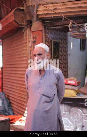 A vertical shot of a Pakistani old male with a white beard in a white topi and kurta on the street Stock Photo