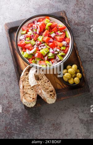 Salad of bell green peppers, tomatoes and onions served with olives and homemade bread close-up on a wooden board on the table. Vertical top view from Stock Photo