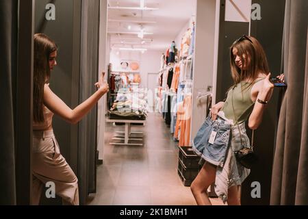 Two teenage girls standing in the changeing room. One of them showing the choice she made the other one likes it Stock Photo