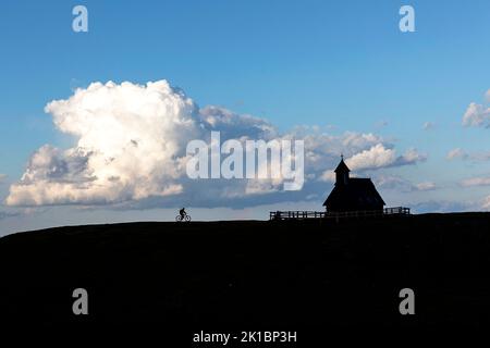 A Mountain biker finishing cycling tour at sunset to the wooden Chapel of Mary of the Snows on Velika Planina plateau near Kamnik, Slovenia Stock Photo