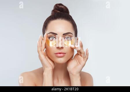 Woman applying golden eye patches. Close up portrait girl. Young woman applying golden collagen patches under eyes, taking care  skin around eyes Stock Photo