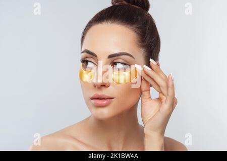 Beautiful woman with healthy perfect skin holds patchs. Beauty face with gold cosmetics collagen hydrogel patch. Lifting anti-wrinkle mask under eyes. Stock Photo