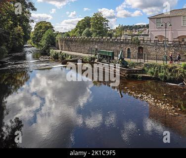 The Weir on the River Tavy at Tavistock seen from the bridge with reflections of the sky. The historic walls and riverside walk towards the Meadows al Stock Photo