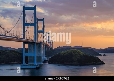 Sunset glow lingers over long suspension bridge between small islands Stock Photo