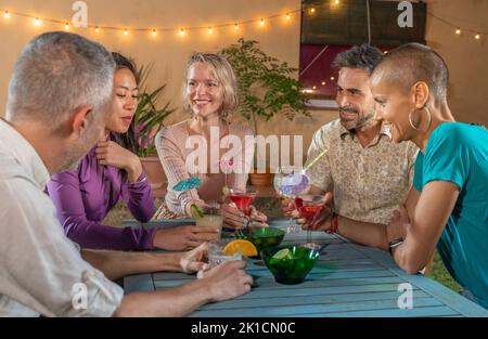 Group of cheerful friends at night party drinking cocktails and having fun together. Smiling people enjoying nightlife drinking alcoholic beverages. Stock Photo