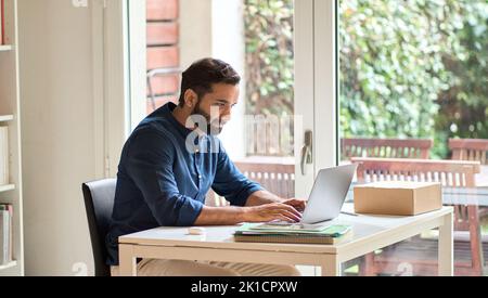 Indian business man remote working on laptop computer sitting at home office. Stock Photo