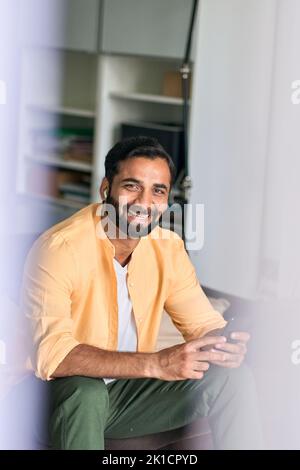 Cheerful indian man sitting at home using mobile phone listening music. Stock Photo