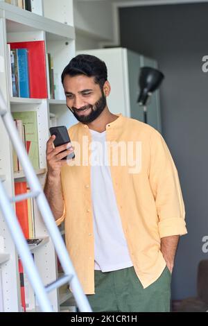Indian man using phone standing at home checking e books in bookshop. Stock Photo