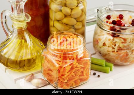 Autumn seasonal pickled or fermented vegetables, mushrooms and olive oil in glass jars on a white wooden board on a light neutral background with garl Stock Photo