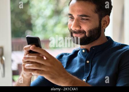 Indian man holding smartphone using mobile phone at home. Stock Photo