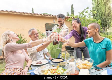Group of cheerful mature friends toasting happy enjoy with big smile around the table at house patio diner. Stock Photo