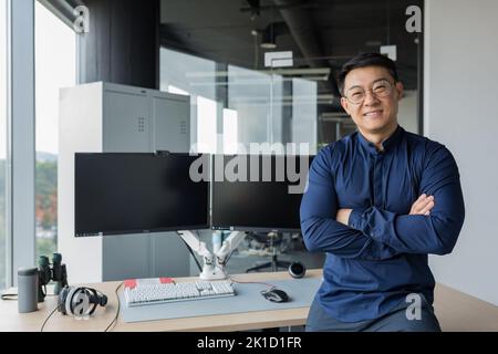 Portrait of successful programmer in modern office of development company, asian man with crossed arms smiling and looking at camera. Stock Photo