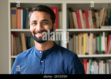 Happy indian business man teacher standing in front of bookshelves, portrait. Stock Photo