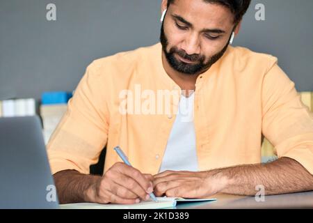Indian man writing notes while learning online business education course. Stock Photo