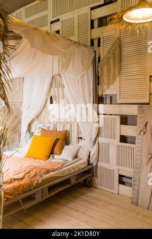 Modern home interior design. Bed with canopy and orange colored pillows, blanket. bedroom interior, scandinavian style.Cozy room in apartment with Stock Photo