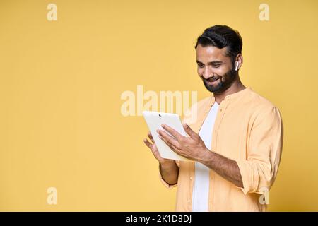 Happy indian man using digital tablet isolated on yellow background. Stock Photo