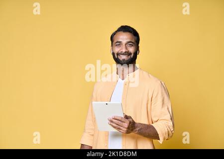 Happy indian man using digital tablet isolated on yellow background. Stock Photo