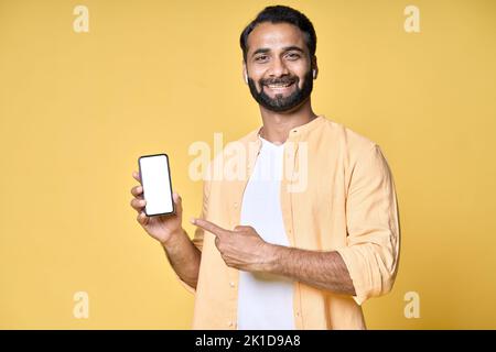 Happy indian man pointing at mobile phone isolated on yellow background. Stock Photo