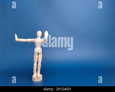 Wooden mannequin posed with one hand in front and the other one on the side on a blue background Stock Photo