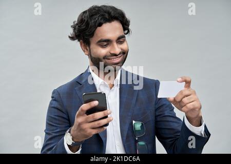 Happy indian arab business man using phone holding credit card. Stock Photo
