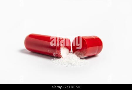 Side view of single red color gel capsule opened, white crystal like powder spilled out, isolated on white background. Pharmaceutical concept. Stock Photo