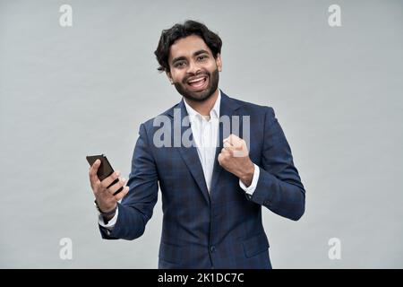 Happy indian business man holding cell phone celebrating win isolated on beige. Stock Photo