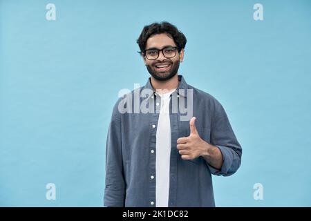 Smiling happy young arab man showing thumbs up isolated on blue background. Stock Photo