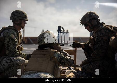 U.S. Navy equipment operator constructionman Ty Mathis and builder petty officer 3rd class Hannah Doge, with 31st Marine Expeditionary Unit, prepare to fire an M240B machine gun during a live fire deck shoot aboard the amphibious dock landing ship USS Rushmore (LSD 47) in the Philippine Sea, Aug. 28, 2022. Marines and Sailors conducted weapons training to further educate their Marines on different weapons platforms. The 31st MEU is operating aboard ships of the Tripoli Amphibious Ready Group in the 7th Fleet area of operations to enhance interoperability with allies and partners and serve as a Stock Photo