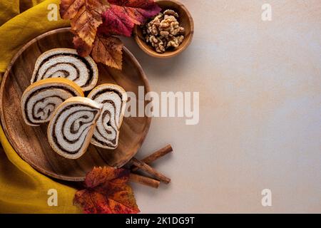 Thanksgiving or autumn dessert background with sliced nut roll on a wooden plate with fall leaves and walnuts Stock Photo