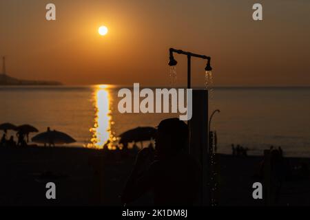 Man silhouette taking shower after swimming at the sea beach. Beautiful view of orange sunset seascape. Summer resort Stock Photo