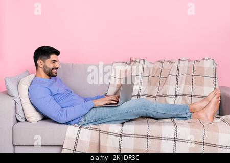 Photo of cute sweet arab guy dressed blue pullover lying couch typing modern device isolated pink color background Stock Photo