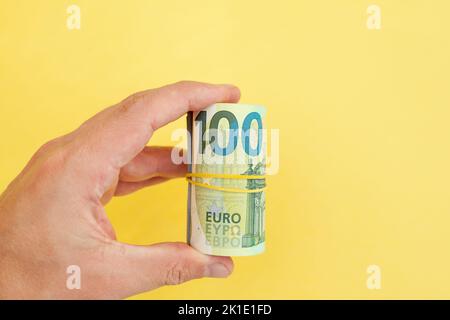 The man holds in his hand money roll of euro banknotes with yellow rubber band on yellow background. cash paper currency, payment, earning and savings Stock Photo