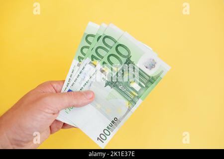 A man holds 100 euro banknotes in his hand on a yellow background. cash paper currency, payment, earning and savings, money and finance concept. Empty Stock Photo