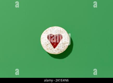 German traditional christmas sweets, linzer cookie, minimalist on a green table. Heart-shaped linzer cookie in bright light. Stock Photo